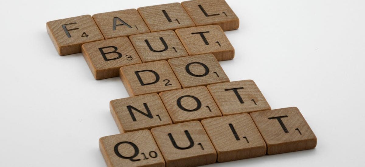 Close-up of Scrabble tiles forming the motivational phrase 'Fail but do not quit' on a white surface.