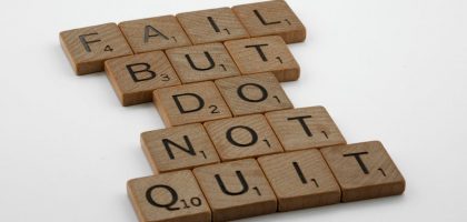 Close-up of Scrabble tiles forming the motivational phrase 'Fail but do not quit' on a white surface.