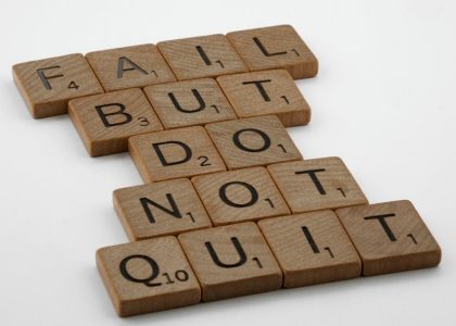 Close-up of Scrabble tiles forming the motivational phrase 'Fail but do not quit' on a white surface.